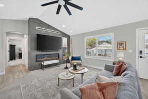 Vaulted living room with a contemporary fireplace feature wall, light wood-finish flooring, and recessed lighting