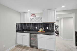 Wet bar featuring white shaker cabinetry, dark countertops, an integrated sink with a matte black faucet, and a beverage refrigerator