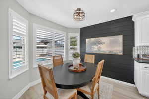 Bay window with plantation shutters, light wood-finish flooring, a shiplap accent wall, white cabinetry, and a black and white tiled backsplash