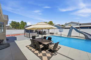 Expansive concrete patio with a built-in outdoor kitchen area, inground swimming pool, and dedicated sports court