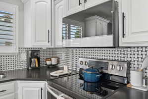 Modern kitchen featuring white cabinetry with black hardware, an over-the-range microwave, and a stainless steel electric range