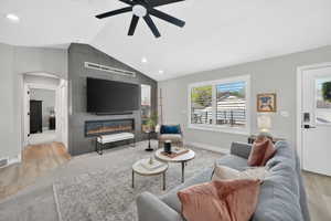 Spacious living area featuring a vaulted ceiling with a ceiling fan, a contemporary fireplace with a sleek surround, wood-finish flooring, and ample natural light from a large window
