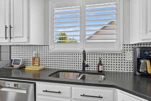 Kitchen featuring white shaker cabinetry, black countertops, stainless steel sink with a matte black faucet, and a basketweave tile backsplash