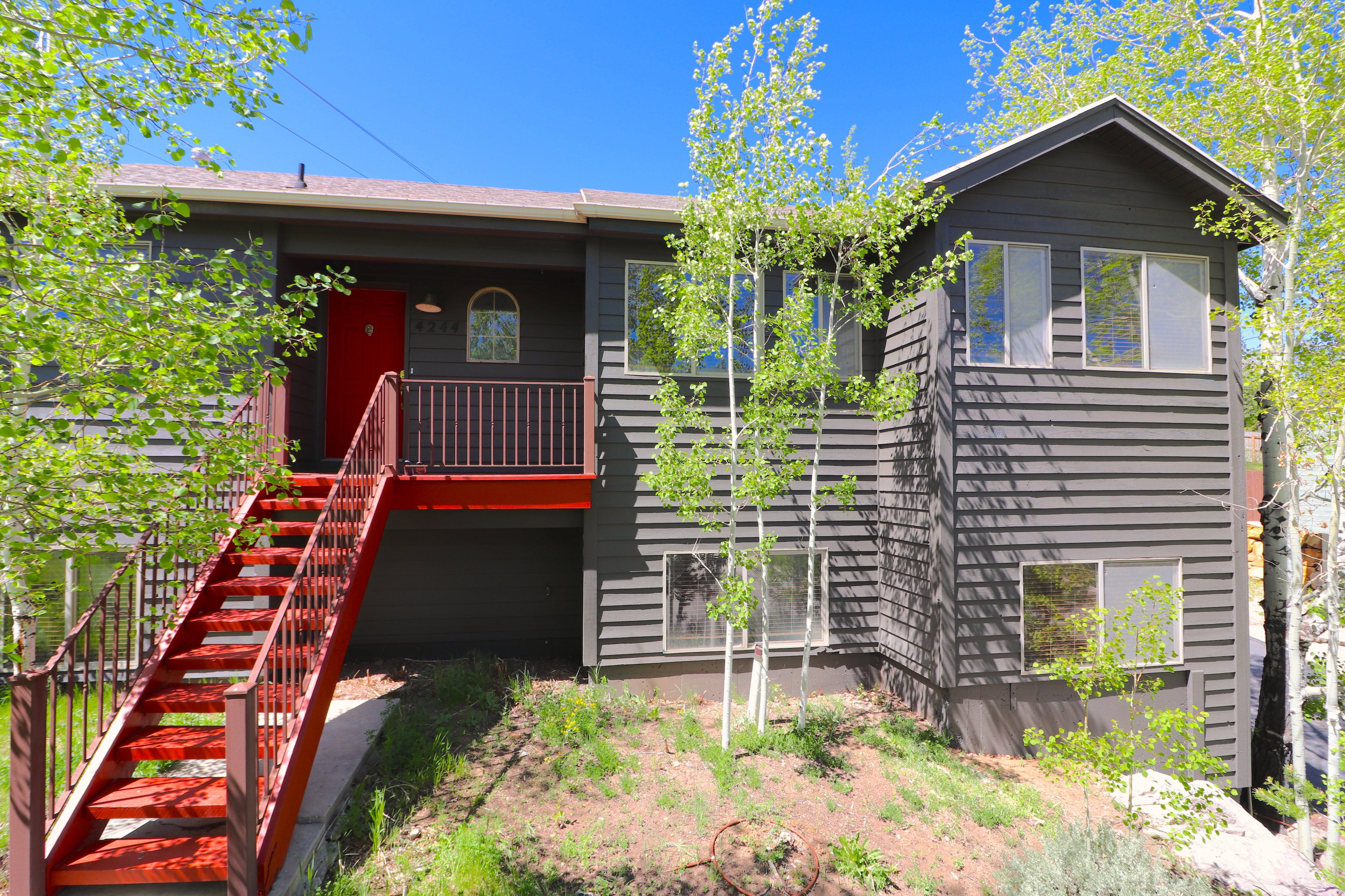 Dark gray horizontal siding exterior with a bright red entry door and a matching red exterior staircase