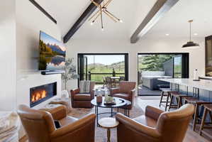 Open-concept living area with a contemporary fireplace, vaulted ceiling featuring exposed beams, and accordion-style glass doors