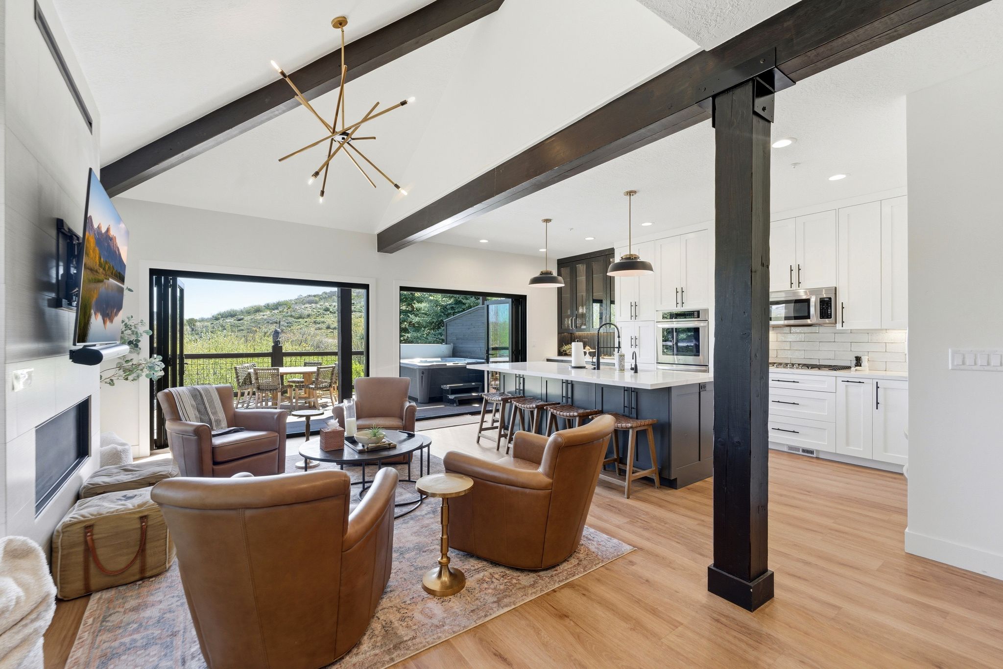 Open-concept living space featuring vaulted ceilings with exposed wood beams, wood-finish flooring, a contemporary fireplace, and a gourmet kitchen with a central island and stainless steel appliances