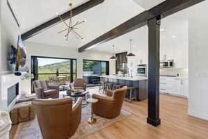 Open-concept living space featuring vaulted ceilings with exposed wood beams, wood-finish flooring, a contemporary fireplace, and a gourmet kitchen with a central island and stainless steel appliances