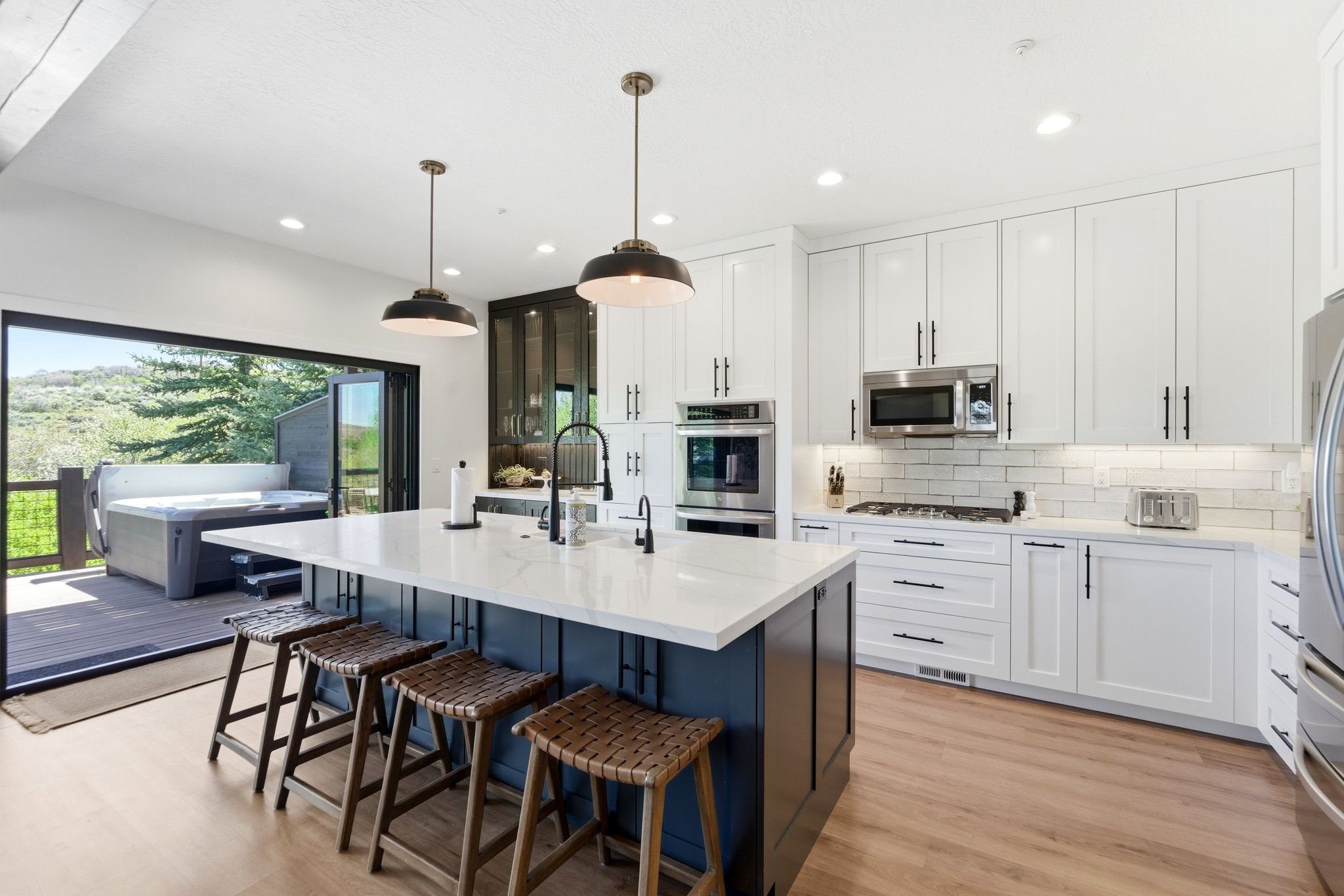 Gourmet kitchen featuring a large island with white countertop, integrated stainless steel appliances, white subway tile backsplash, and wood-finish flooring