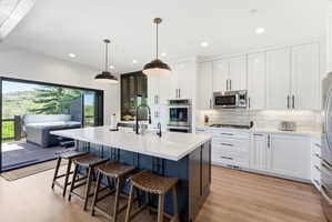 Gourmet kitchen featuring a large island with white countertop, integrated stainless steel appliances, white subway tile backsplash, and wood-finish flooring