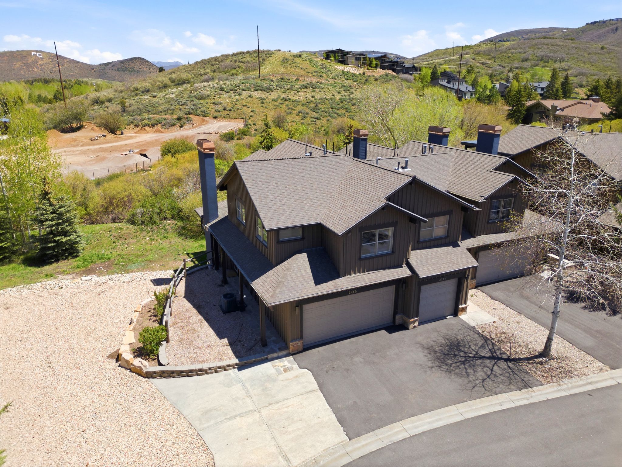 Multi-level residence featuring a brown siding exterior, a dark shingle roof, and multiple chimneys with stone accents