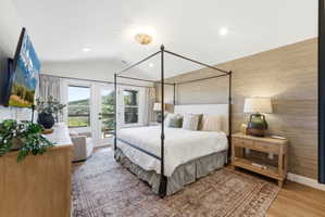 Bedroom with vaulted ceiling, wood-finish flooring, and a textured accent wall