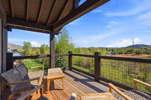 Covered outdoor deck with wood-finish flooring, dark wood railings, and mesh infill