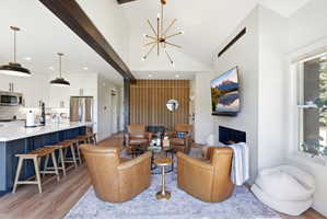 Open concept living area featuring vaulted ceilings with exposed beams, a contemporary fireplace, and wood-finish flooring