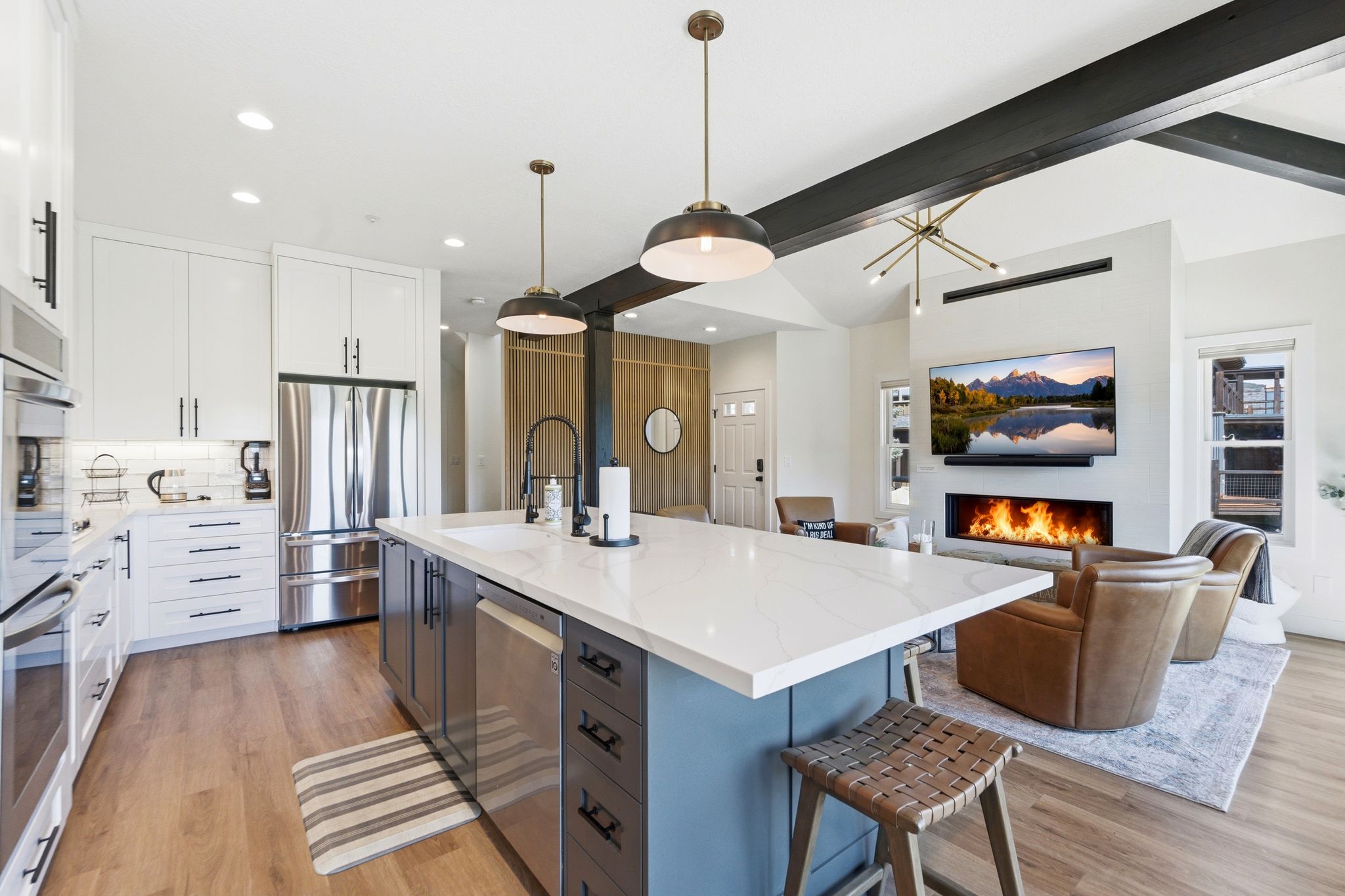 Open-concept kitchen and living area featuring a large center island with a white countertop and seating, stainless steel appliances, and wood-finish flooring