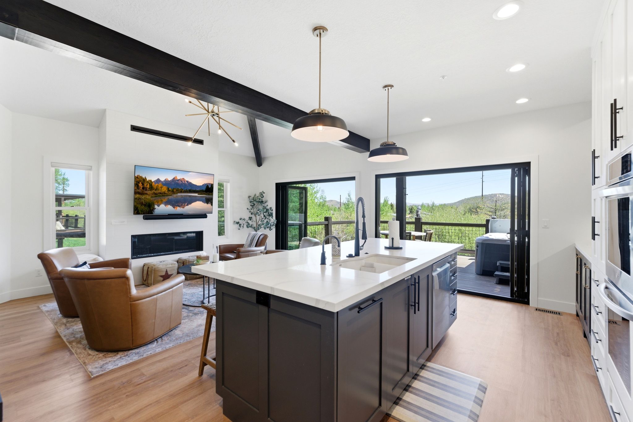 Open-concept kitchen and living area featuring wood-finish flooring, a kitchen island with sink, integrated dishwasher, and pendant lighting