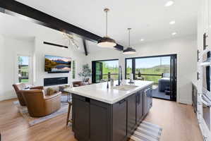 Open-concept kitchen and living area featuring wood-finish flooring, a kitchen island with sink, integrated dishwasher, and pendant lighting