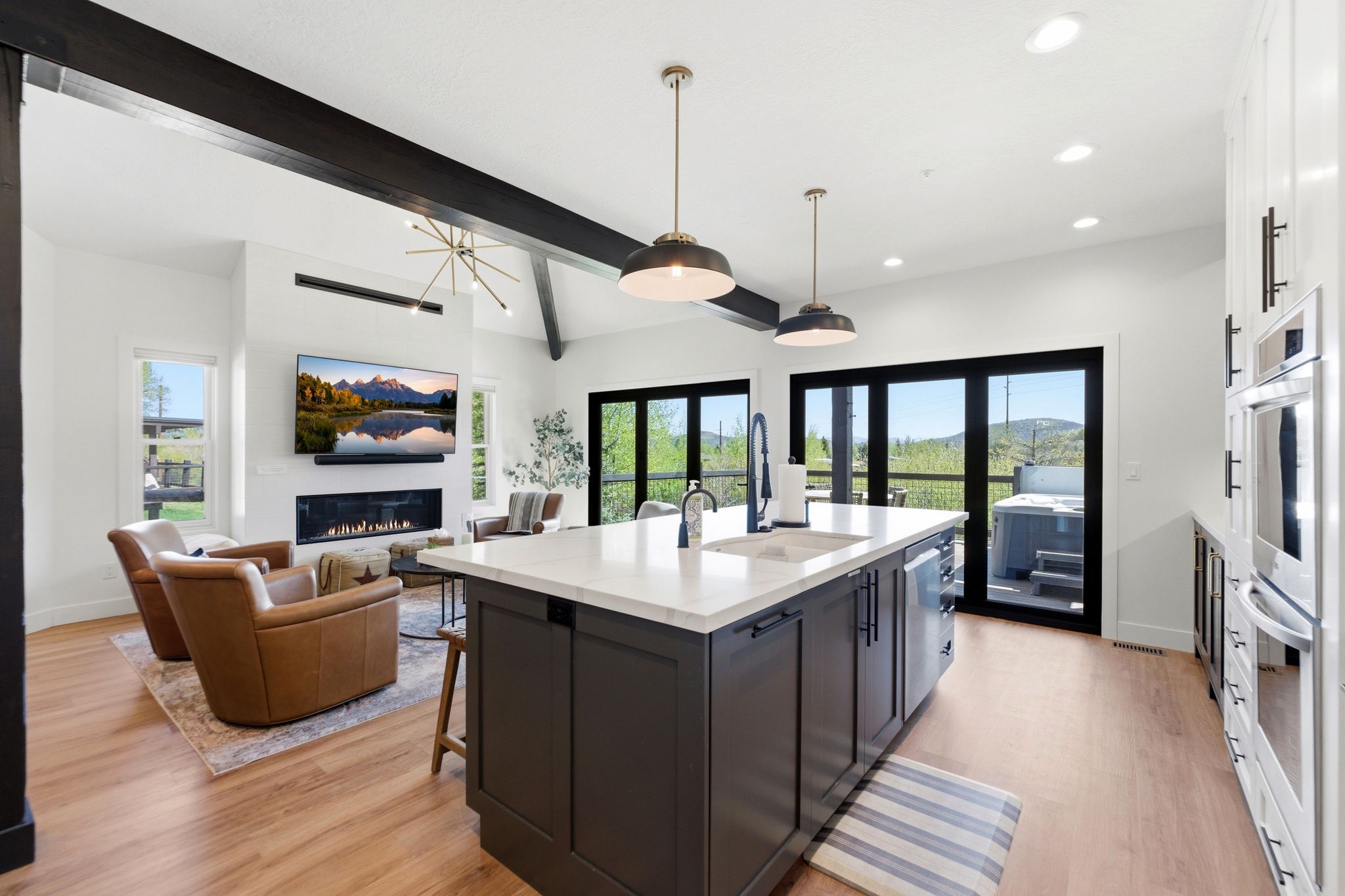 Open-concept living space featuring a central kitchen island with a white countertop and dark cabinetry, wood-finish flooring, and a linear fireplace