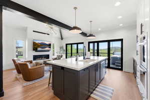 Open-concept living space featuring a central kitchen island with a white countertop and dark cabinetry, wood-finish flooring, and a linear fireplace