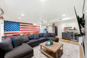 Spacious entertainment room featuring a full wall brick accent, recessed lighting, wood-finish flooring, and a built-in wet bar with a beverage cooler and dark cabinetry