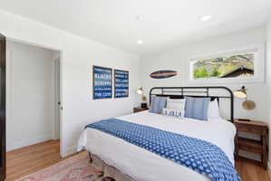 Bright bedroom featuring wood-finish flooring, recessed lighting, and a panoramic window showcasing a mountain backdrop