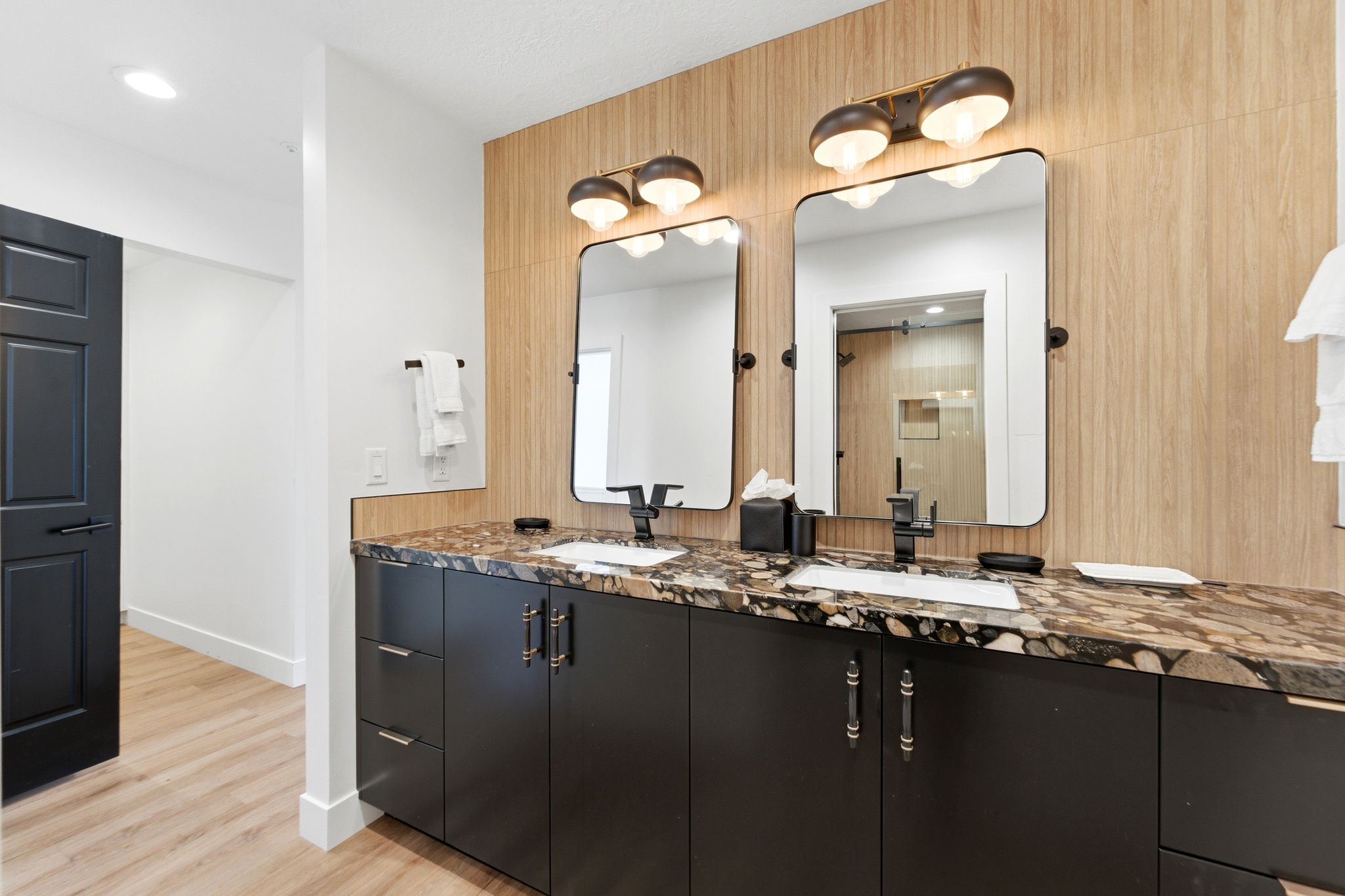 Dual vanity featuring dark cabinetry with decorative hardware, a patterned stone countertop, and two rectangular mirrors with integrated lighting