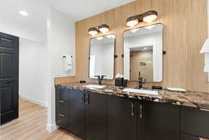 Dual vanity featuring dark cabinetry with decorative hardware, a patterned stone countertop, and two rectangular mirrors with integrated lighting