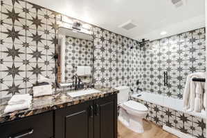 Bathroom featuring a patterned tile surround, dark wood vanity with a stone countertop, a rectangular undermount sink, and a framed mirror