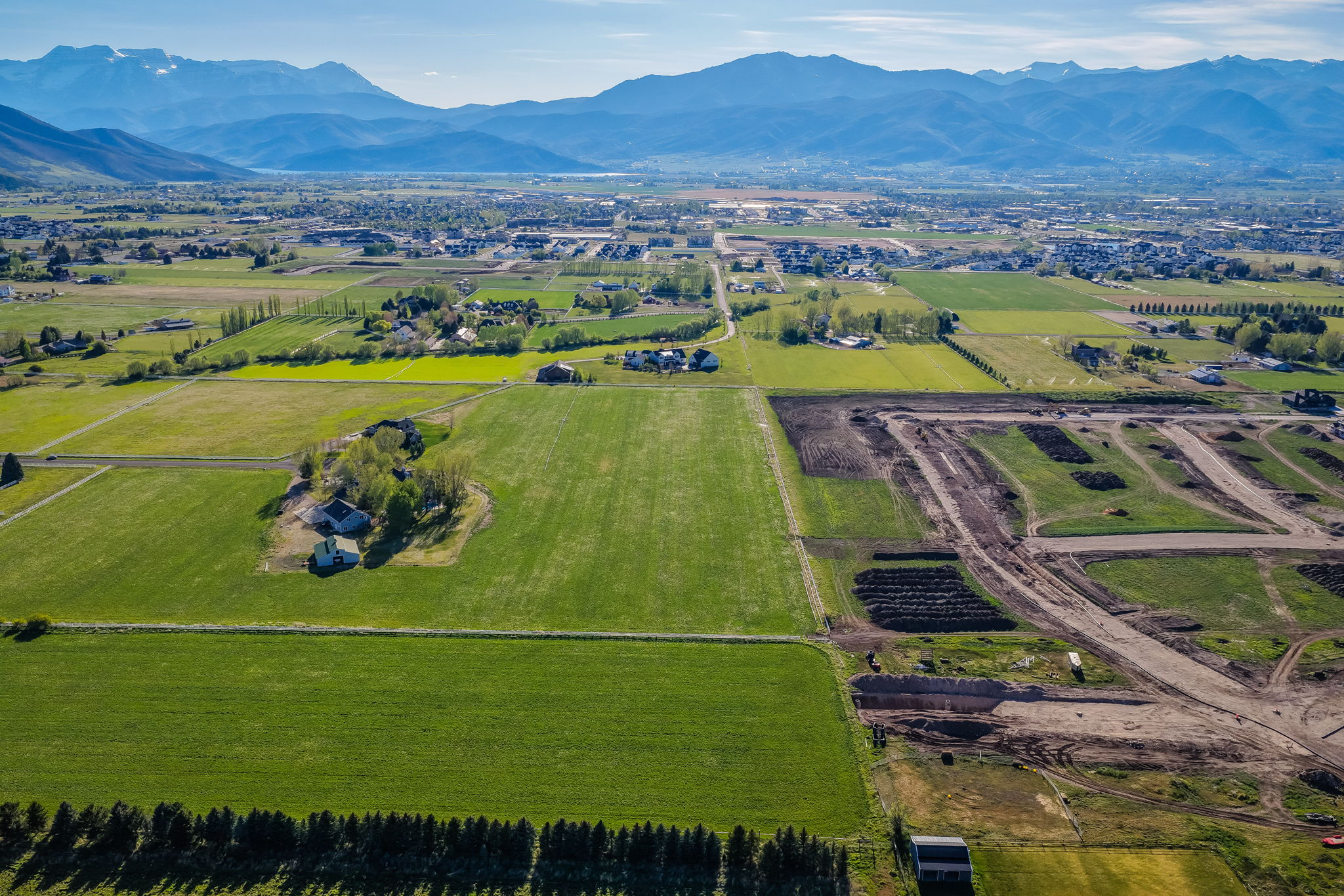 Expansive agricultural landscape featuring green fields, distant mountains, and developing infrastructure