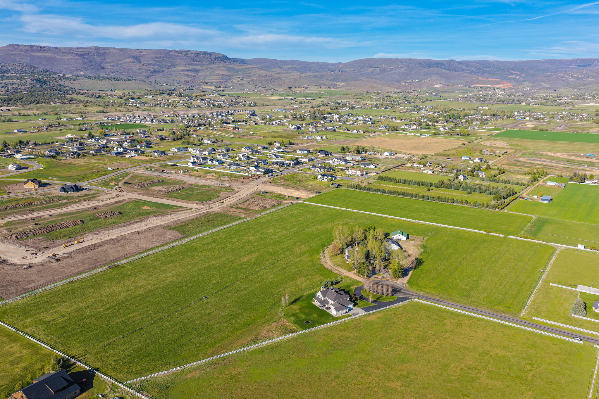 Expansive land parcel featuring open fields, a paved roadway, and distant mountainous terrain