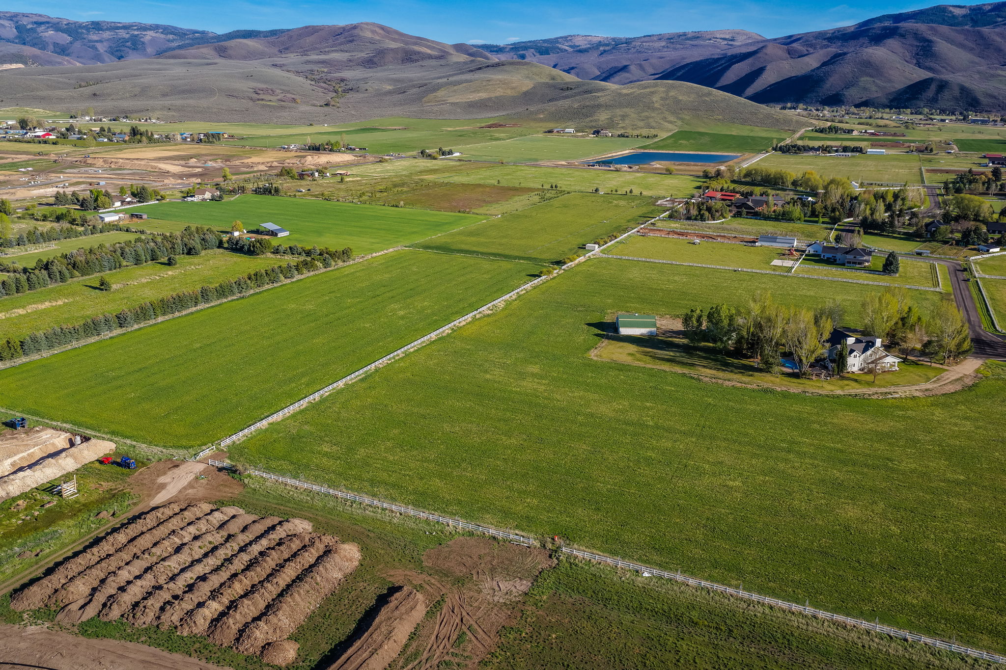 Expansive agricultural land featuring a verdant field, mountain backdrop, and multiple building sites