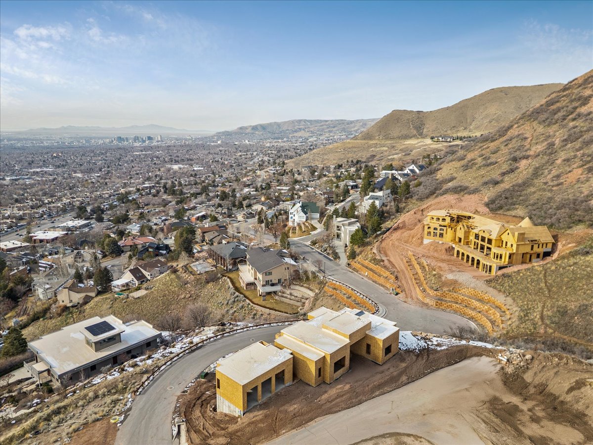 Expansive hillside development featuring multiple properties under construction, a paved winding road, and retaining walls