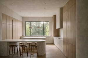 Kitchen featuring light wood-finish cabinetry, curved stone islands, integrated appliances, and a large picture window