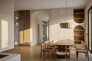 Open concept interior featuring light wood-finish flooring, a wall of built-in cabinetry, integrated arched shelving, a large dining table, and dark-framed windows