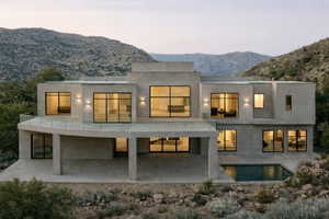 Contemporary stucco exterior featuring a curved balcony with glass railing, an integrated ground-level patio, multiple large windows, and a rectangular plunge pool