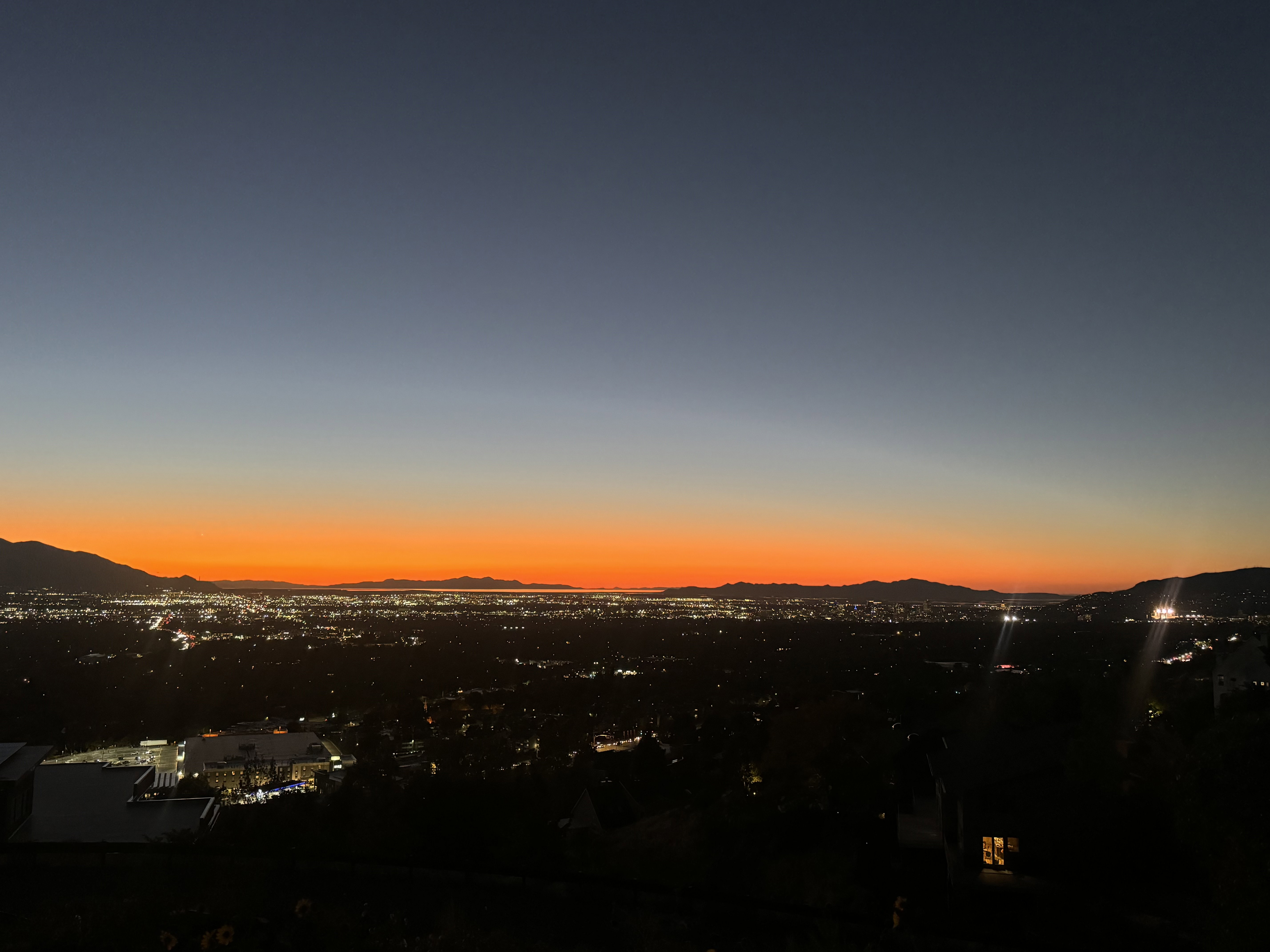 Expansive cityscape with distant mountains under a vibrant orange and blue twilight sky