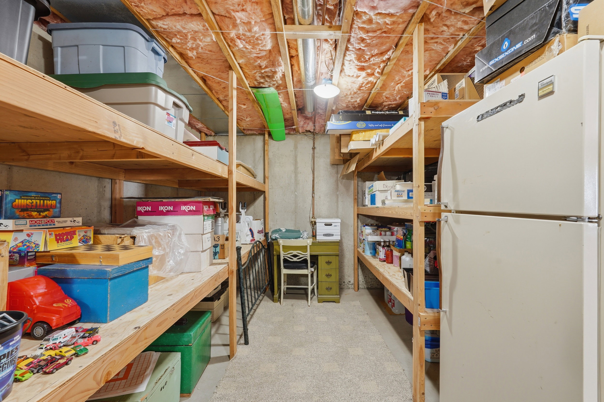 Basement storage area featuring extensive built-in wooden shelving and extra fridge