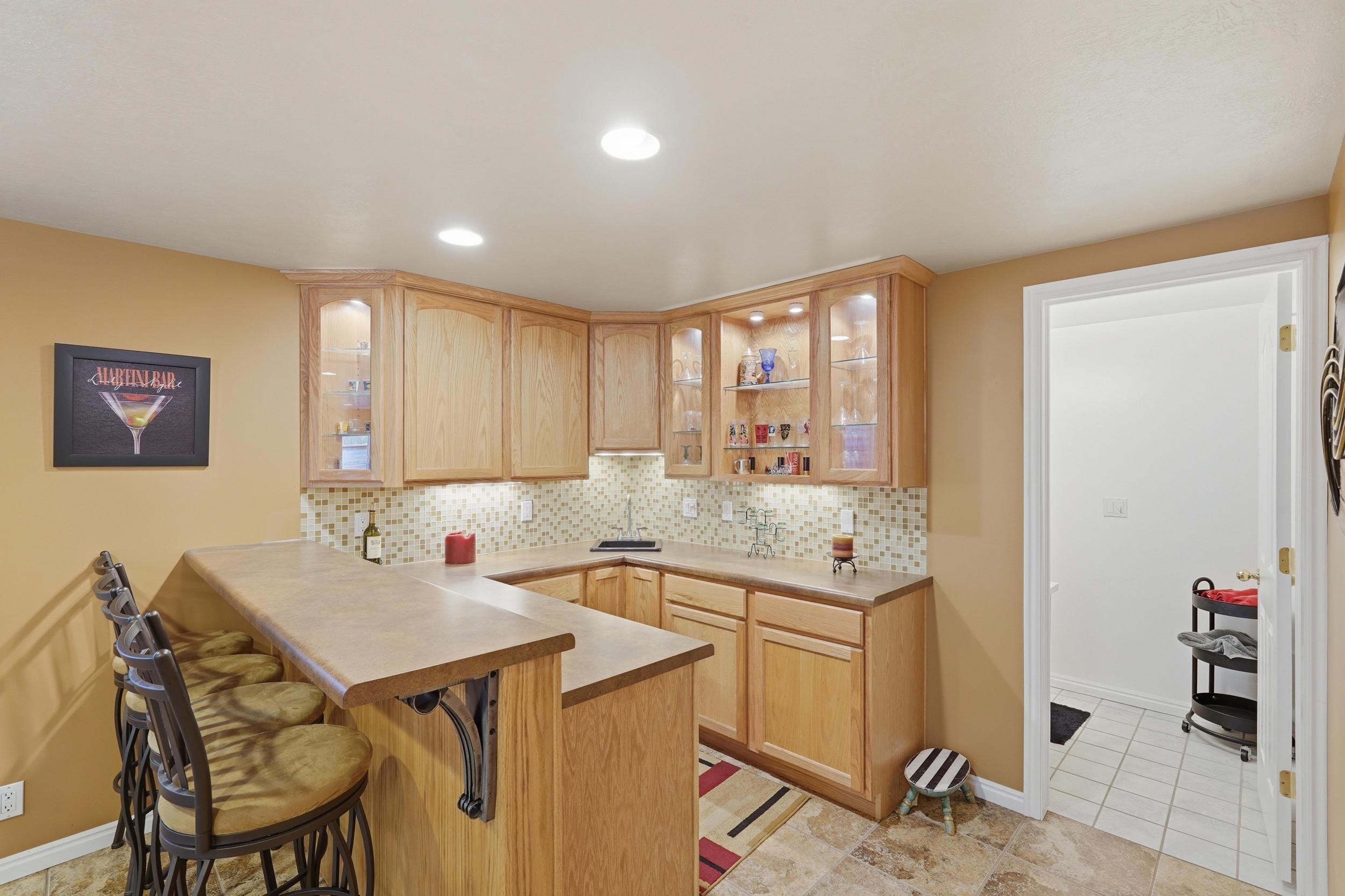 Built-in bar featuring wood-finish cabinetry, glass-front upper cabinets with integrated lighting, and a mosaic tile backsplash