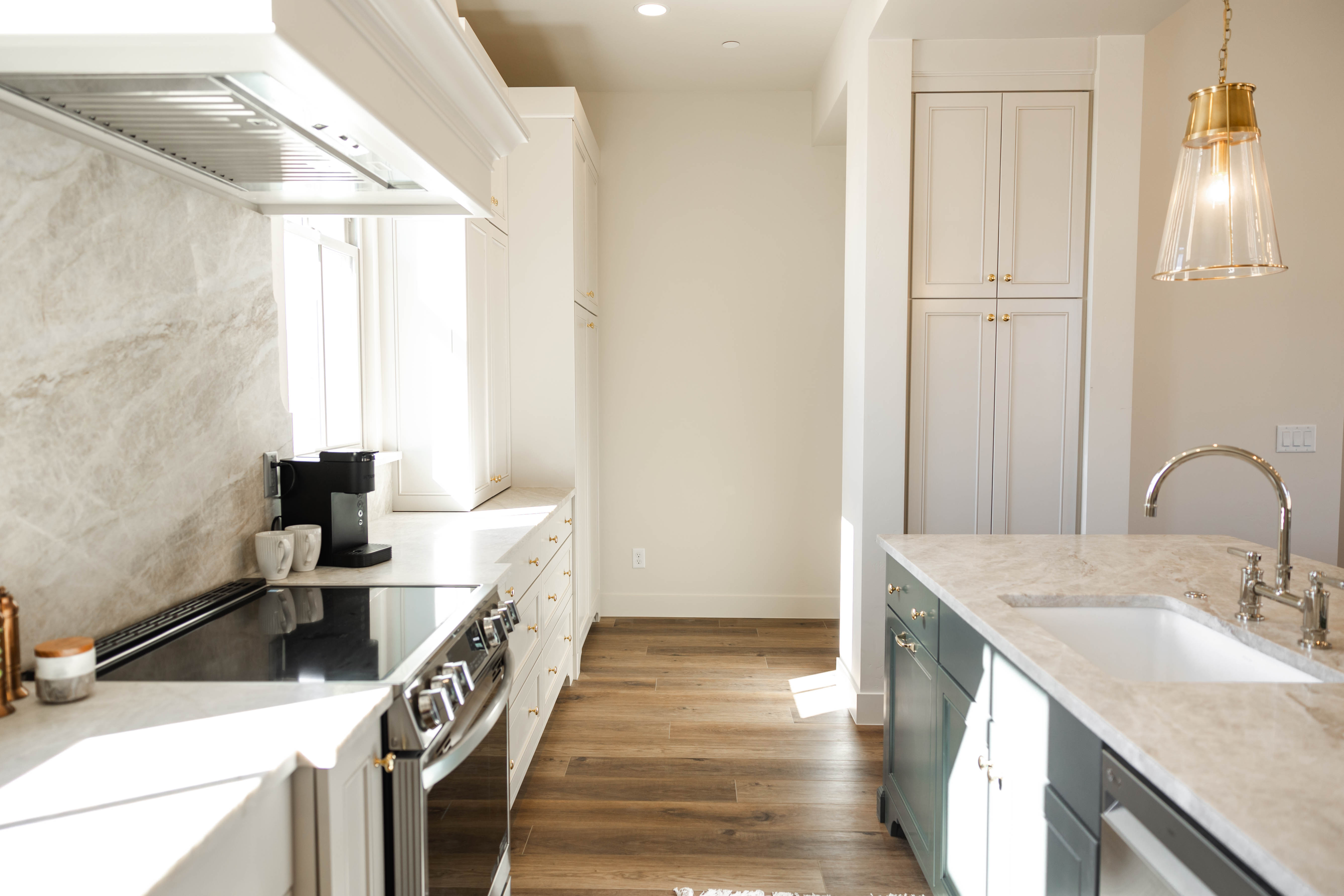 Modern kitchen featuring an integrated electric range, full-height decorative backsplash, white upper and lower cabinetry, and a central island with an undermount sink