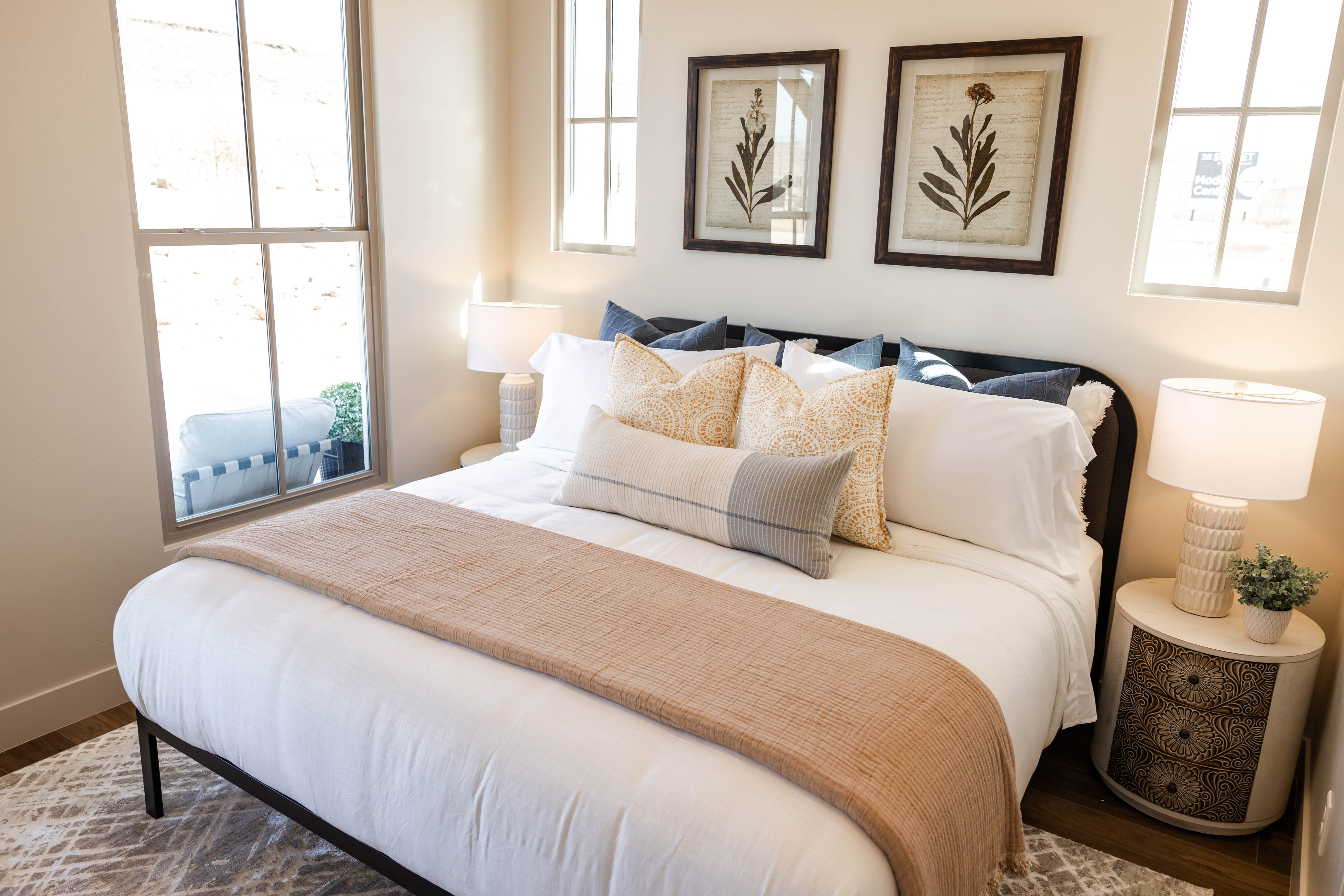 Bedroom featuring light-toned walls, wood-finish flooring, two large windows, and a dark-framed headboard