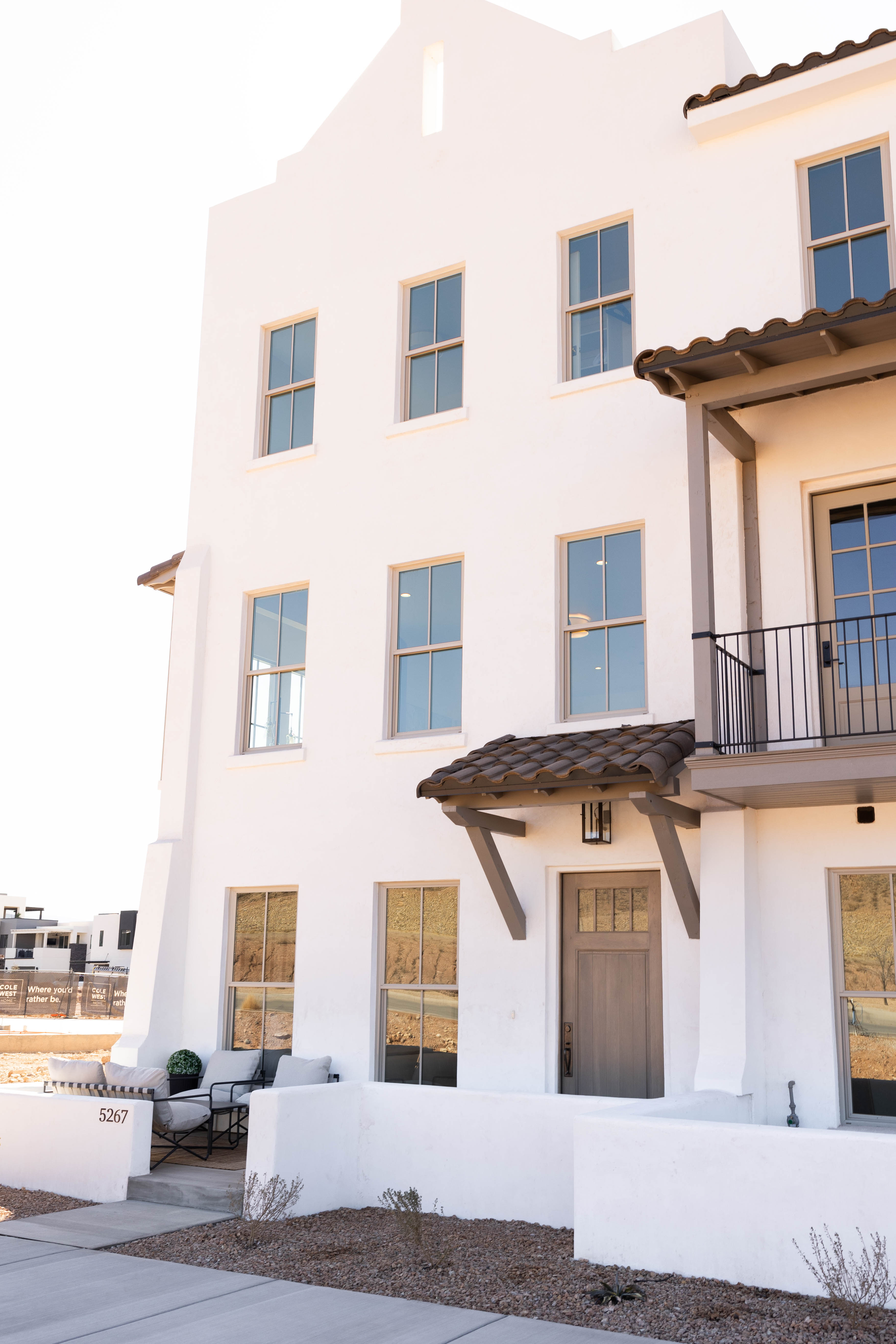 Spanish Colonial-inspired exterior featuring a stucco finish, multiple double-hung windows, a prominent wood-panel entry door, and an overhead tile awning