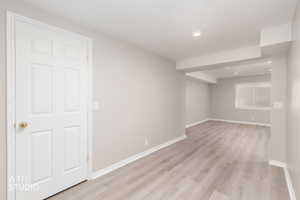 Neutral-toned interior featuring recessed lighting, a white six-panel door with brass hardware, and light wood-finish flooring