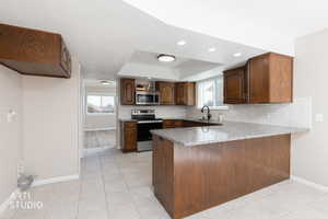 Kitchen featuring a breakfast bar with granite-look countertop, wood-finish cabinetry, stainless steel appliances, and tile flooring