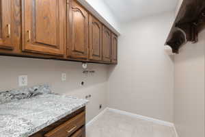 Laundry area featuring wood cabinetry with brass hardware, a light-toned patterned countertop, light neutral wall paint, and ceramic tile flooring