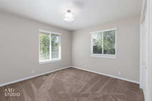 Neutral-toned room featuring two windows with horizontal blinds, a flush-mount ceiling light fixture, and textured carpeting