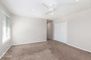 Spacious carpeted room featuring a white ceiling fan, recessed lighting, a window with blinds, and bi-fold closet doors