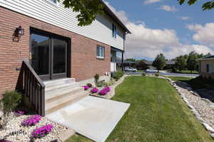 Brick and siding exterior featuring a patio with concrete steps, dark-framed glass doors, and manicured landscaping with flowering plants and rock beds