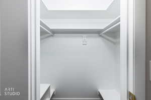 Spacious closet featuring white painted walls, upper shelving, a hanging rod, and two lower shelves
