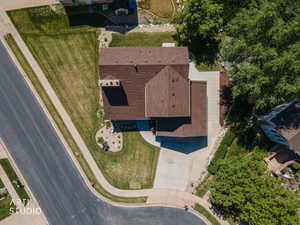 Property featuring a brown shingle roof, expansive front lawn, paved driveway, and mature landscaping