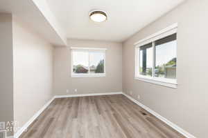 Bright room featuring two windows, wood-finish flooring, white baseboards, and a flush-mount ceiling light