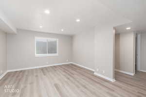 Spacious room featuring light wood-finish flooring, recessed lighting, neutral wall tones, and a window with blinds